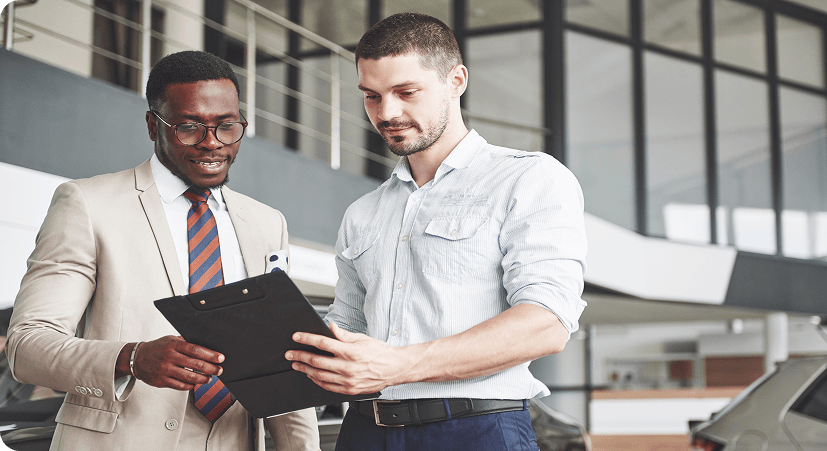 Two men are standing together and reviewing paperwork