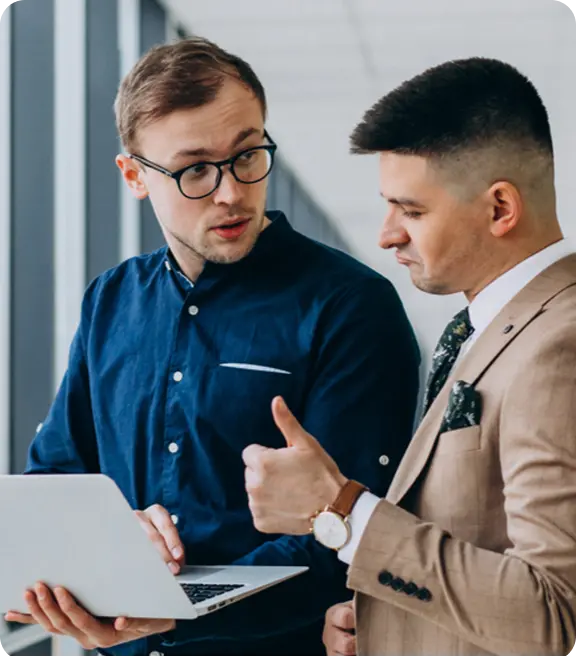 Two business professionals in formal attire focused on a laptop, engaged in a discussion.