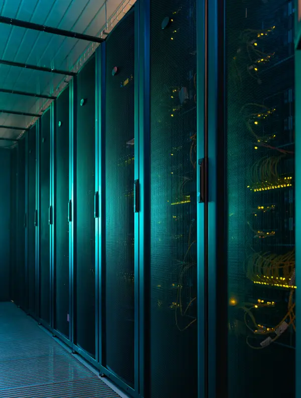 A row of dark server racks illuminated by bright teal and yellow lights in a data center