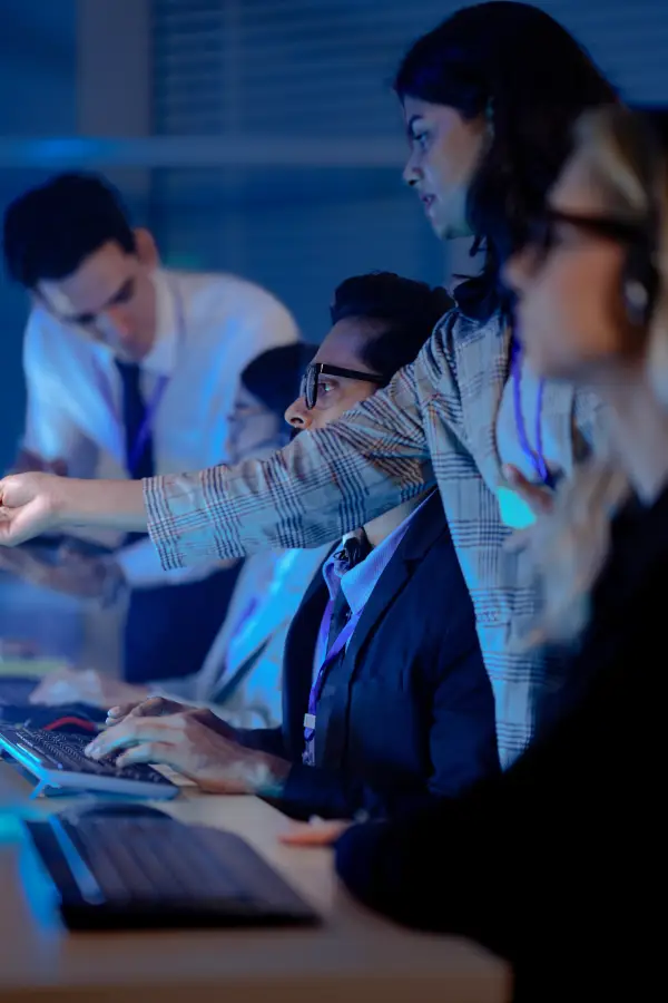 Group of diverse customer service representatives wearing headsets and working on computers in a blue-lit office