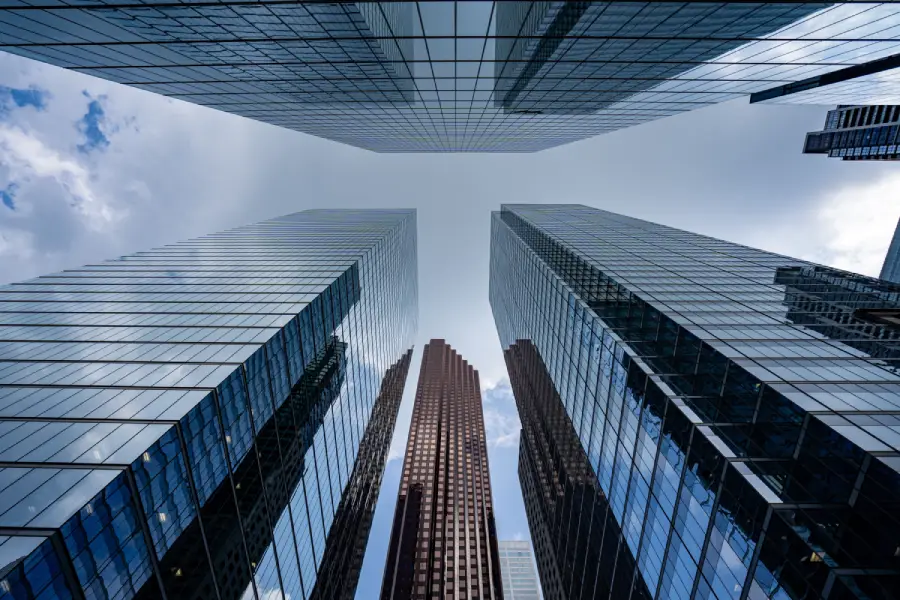 View looking up at several tall skyscrapers with reflective glass windows against a blue sky with clouds.