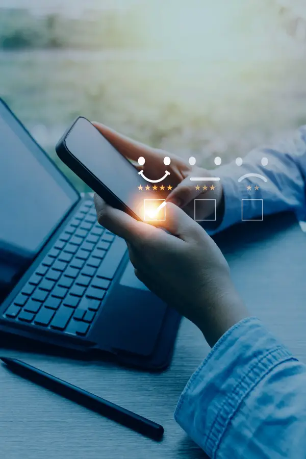 A person using a smartphone displaying a 5-star rating and a smiling face icon, leaving positive feedback