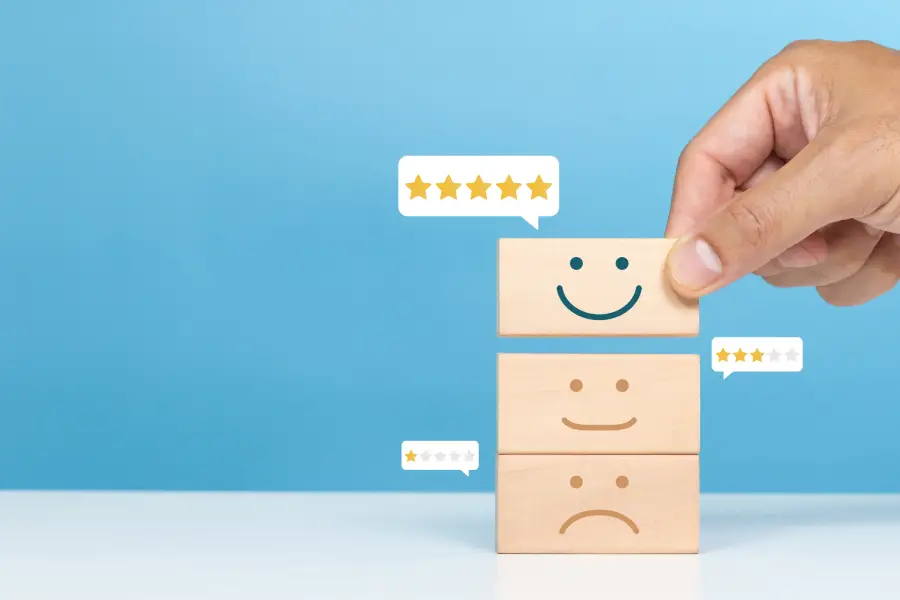 A hand placing a wooden block with a smiling face on top of blocks with neutral and sad faces, representing customer satisfaction ratings