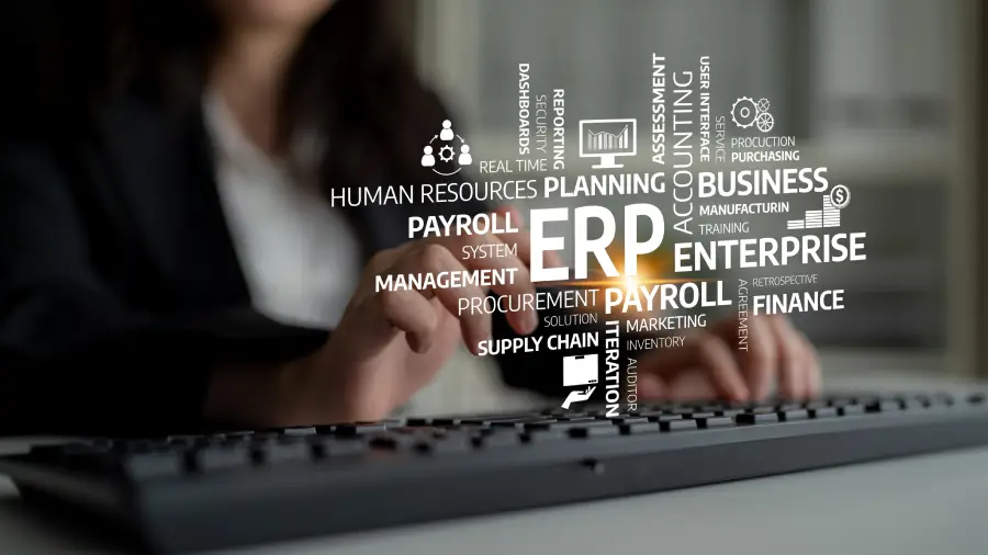 Person typing on a keyboard with a digital word cloud related to ERP, such as payroll, supply chain, and human resources