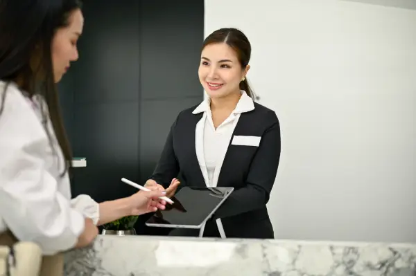 A smiling hotel receptionist presenting a digital tablet to a guest at the front desk