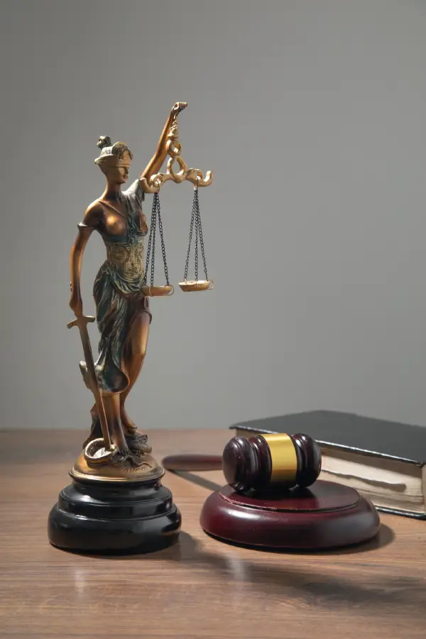 A bronze statue of Lady Justice holding scales next to a wooden gavel and a law book