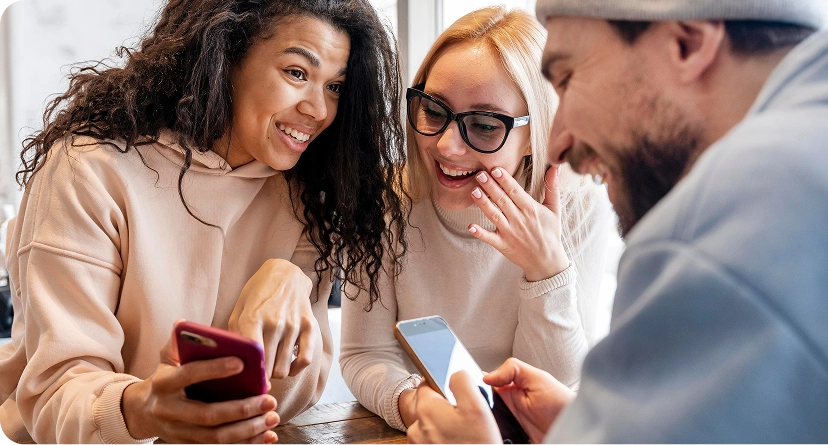 Three people gathered together around a table, smiling and looking at smartphones