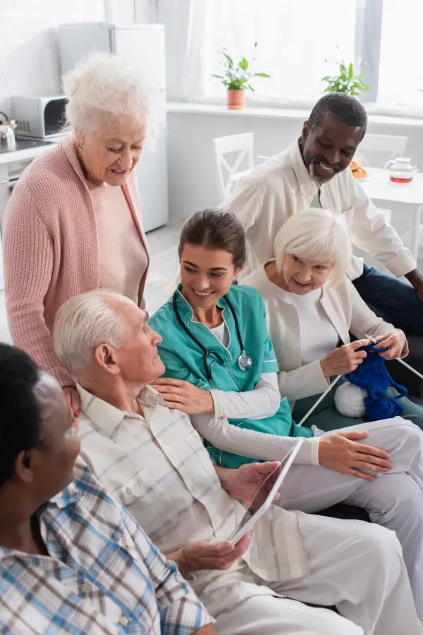 Group of diverse elderly people and a caregiver looking at a tablet together in a bright room