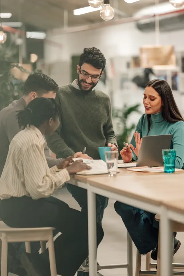 Group of diverse coworkers having a discussion over a laptop and notebooks at a wooden desk in a modern office